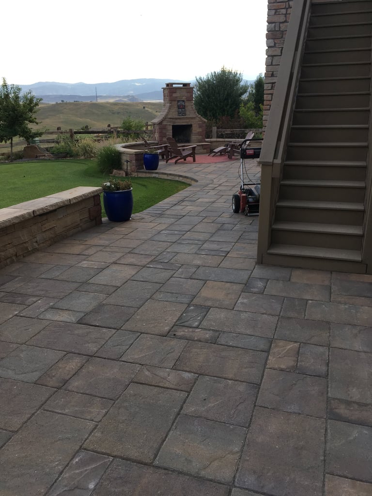 Backyard patio with stone pavers, outdoor fireplace, seating area, manicured lawn, and mountain views in the distance