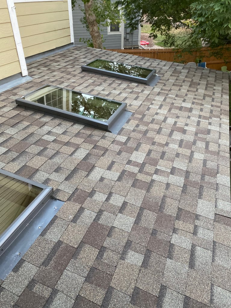 Residential roof with asphalt shingles, two skylight windows, and metal trim installed during construction or renovation