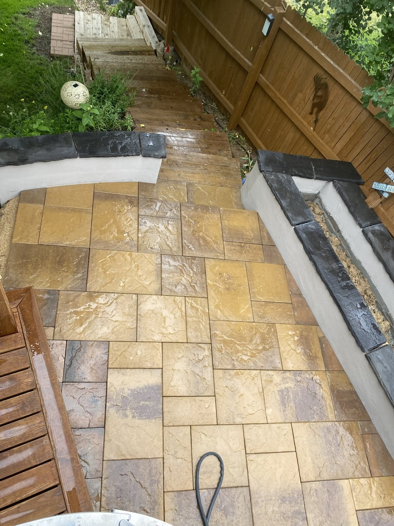 Overhead view of a patio with golden stone tiles, wet from rain, adjacent to a wooden deck and garden area