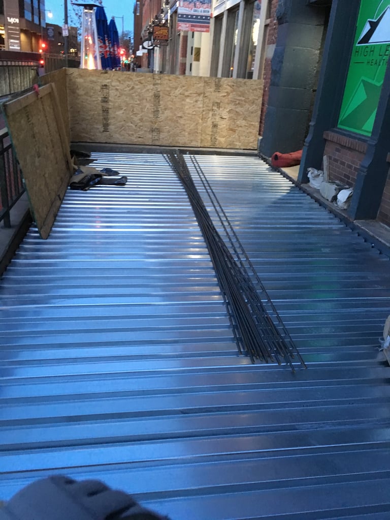Urban alley with blue metal corrugated flooring and wooden walls, city buildings visible in background at dusk