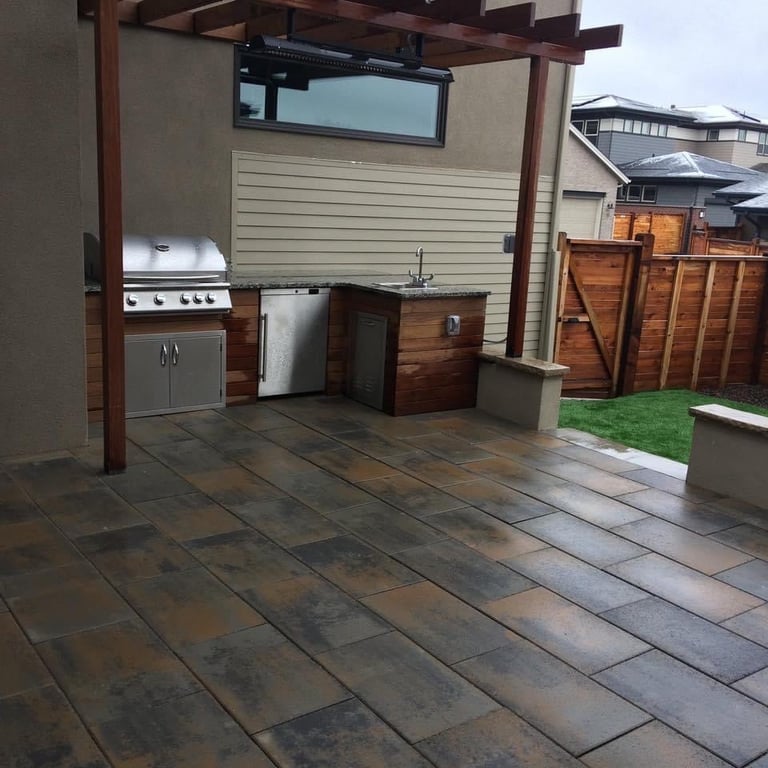 Modern covered patio with outdoor kitchen featuring stainless steel appliances, wooden cabinetry, and dark tile flooring under a pergola