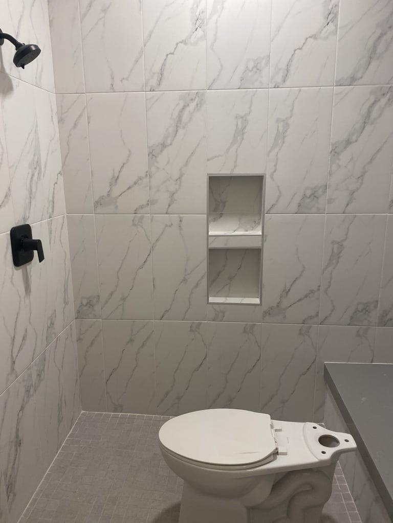 Modern bathroom with marble-patterned tile walls, white toilet with bidet seat, recessed shelf, and black fixtures