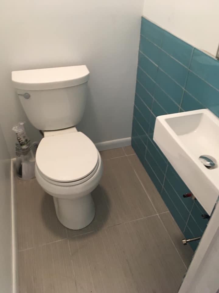 Small bathroom with white toilet, white pedestal sink, and teal subway tile backsplash on gray tile floor