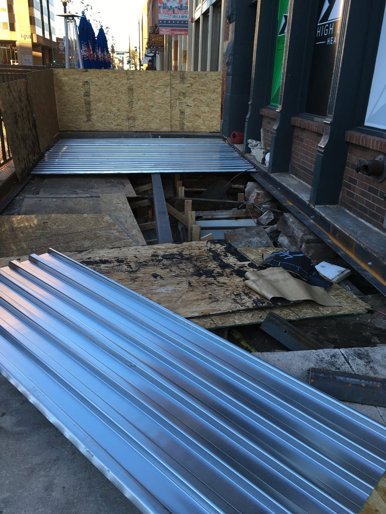 Metal truck bed panels and frame components laid out on pavement in industrial alley with construction barriers
