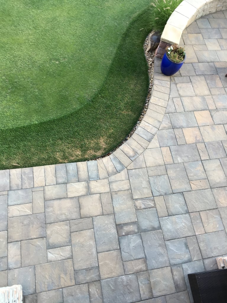 Overhead view of a curved patio with patterned stone pavers adjoining a green lawn and flower bed