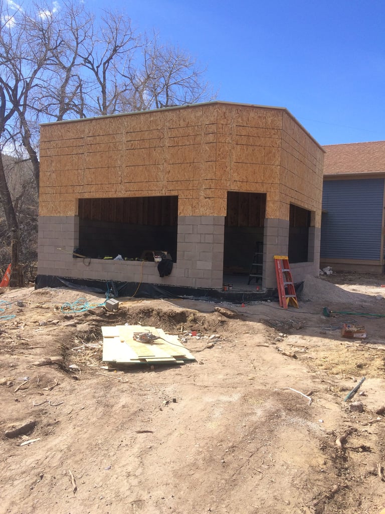 New brick house under construction with concrete block foundation and open garage openings, surrounded by dirt and construction materials