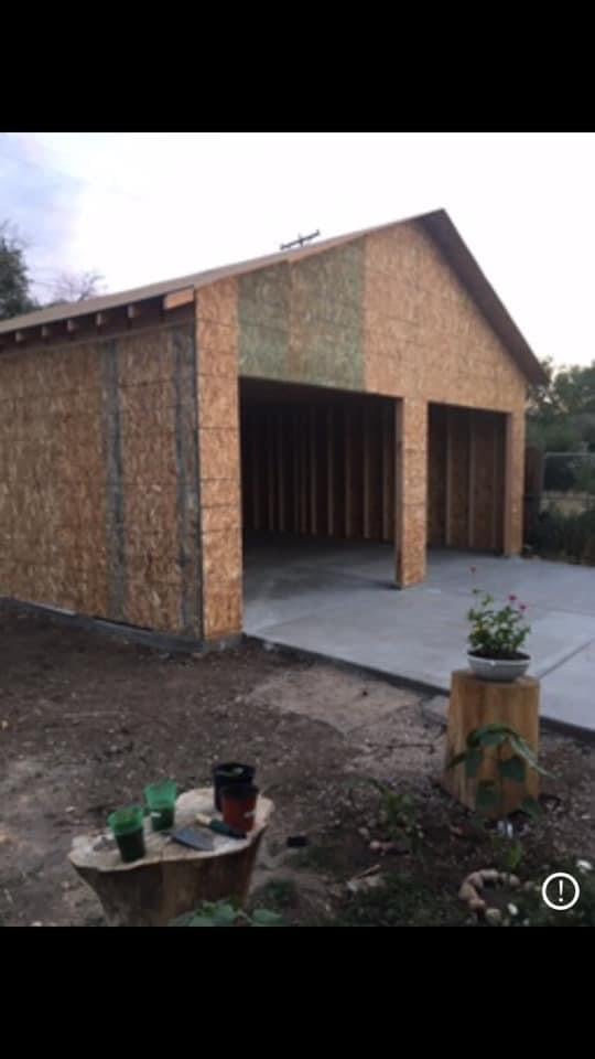New brick garage with open double bay doors and concrete pad, potted plants in front yard