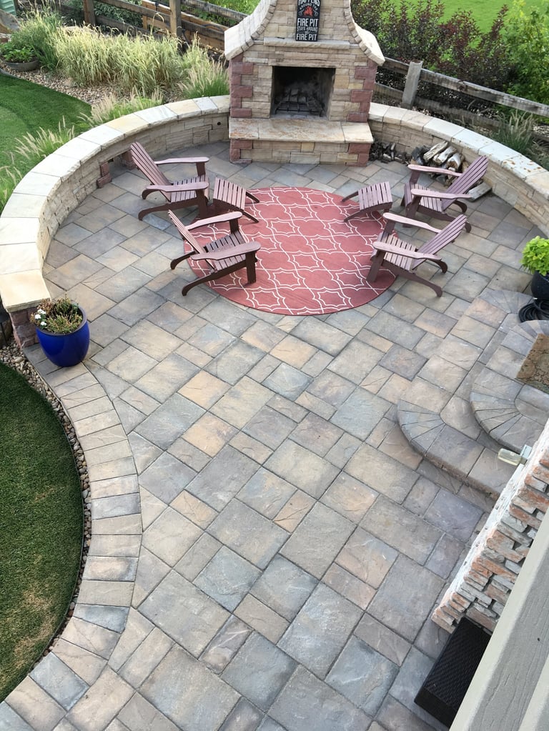 Aerial view of a patio with red rug, burgundy chairs, fireplace, and curved stone walls surrounded by landscaping