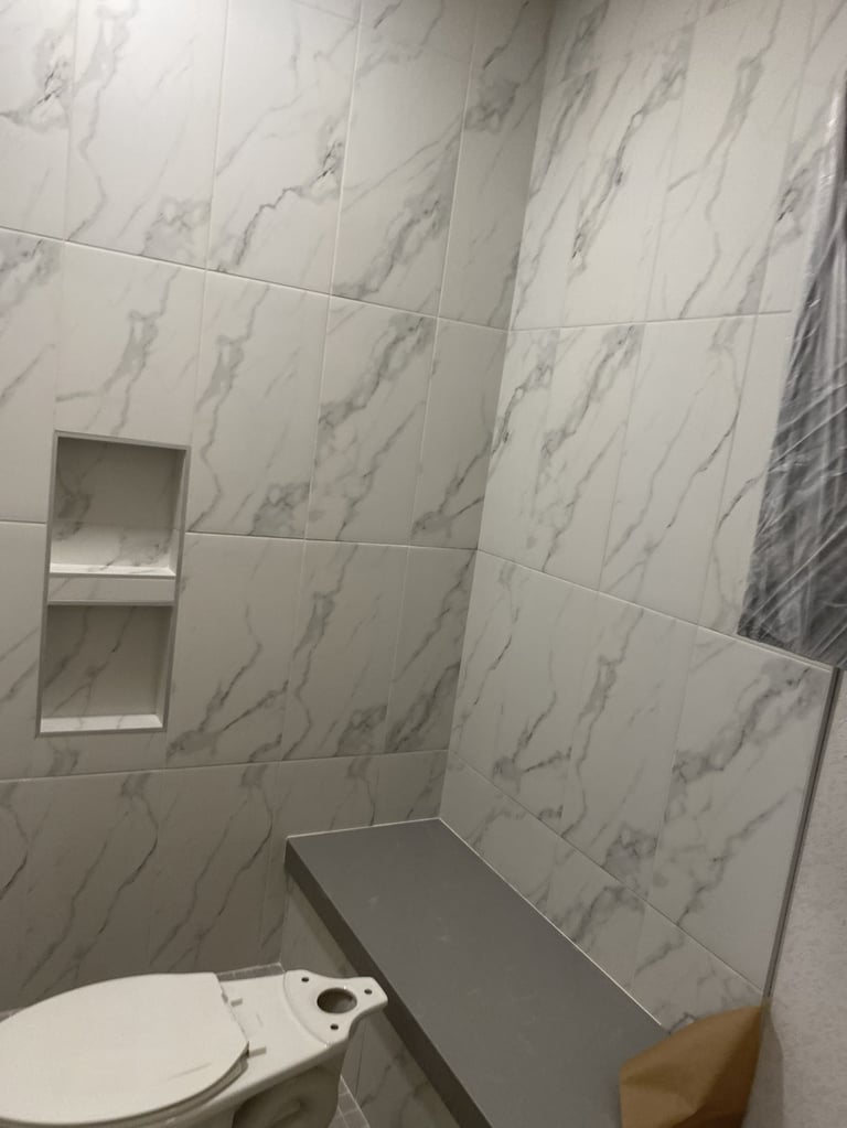 Modern bathroom shower area with marble-textured white and gray tile walls, built-in shelving niche, and bench seating