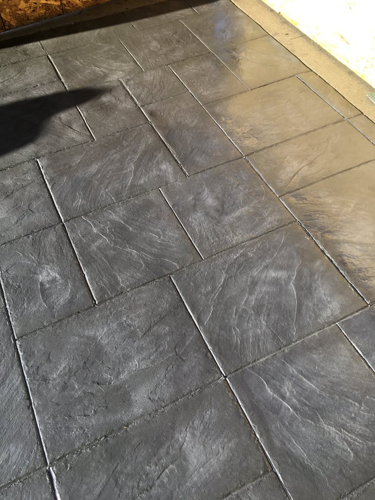 Close-up of dark slate tile flooring with grout lines in a diagonal herringbone pattern, showing texture and variation in the stone surface