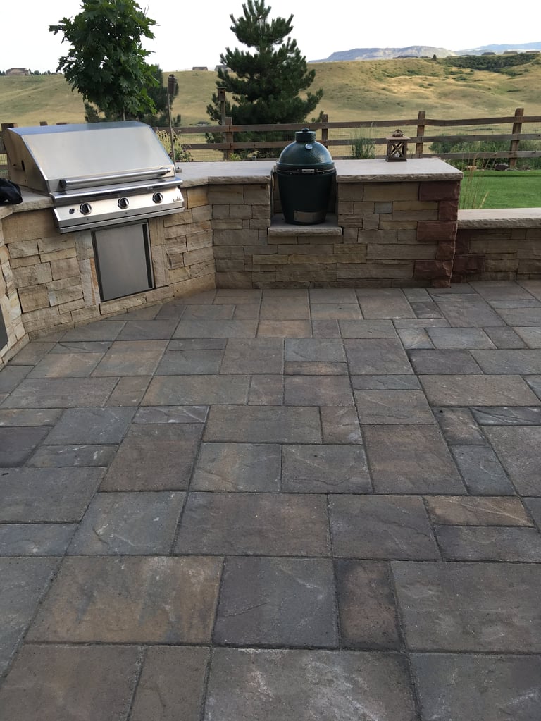 Outdoor kitchen with gas grill and black smoker built into stone counters on a slate patio with rolling hills in background