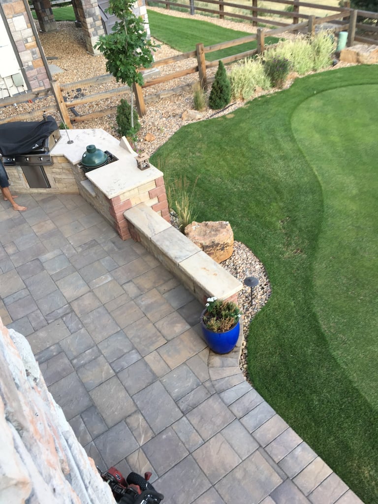 Aerial view of backyard garden with paved patio, raised brick planter bed, manicured lawn, and wooden fencing
