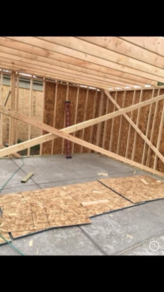 Interior of wooden framed construction showing exposed studs, concrete foundation, plywood flooring, and window opening in early building stage