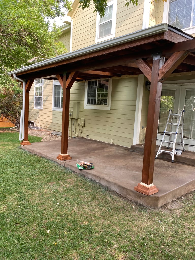 Wooden pergola attached to tan house with concrete patio and lawn, ladder leaning against wall