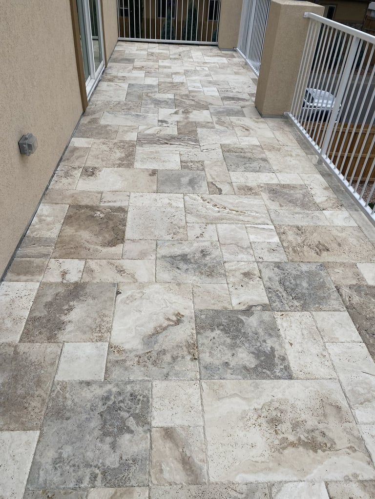 Outdoor patio with travertine tile flooring in varied earth tones, flanked by white metal railings on both sides