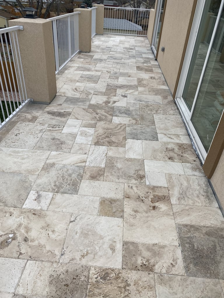 Modern patio with light stone tile flooring, white railings, glass doors, and cream-colored building walls
