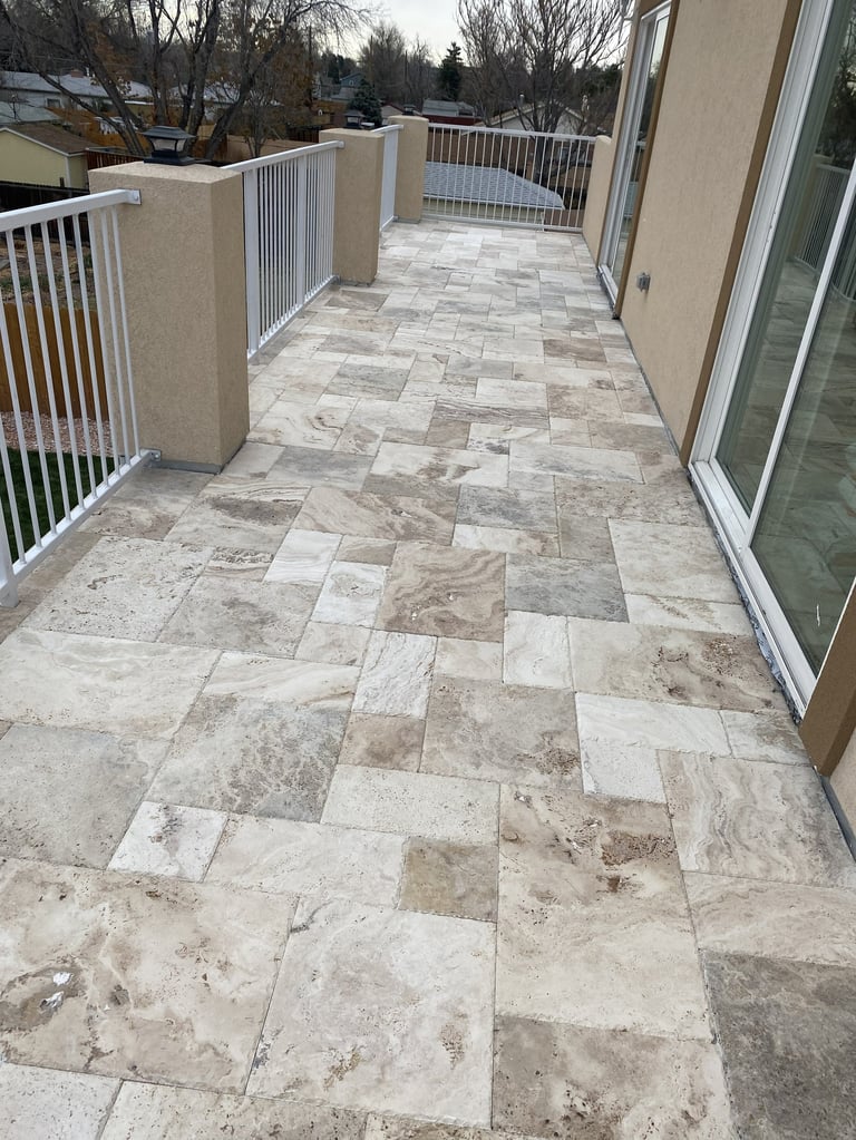 Outdoor deck with stone tile flooring in neutral tones and white metal railings overlooking residential neighborhood